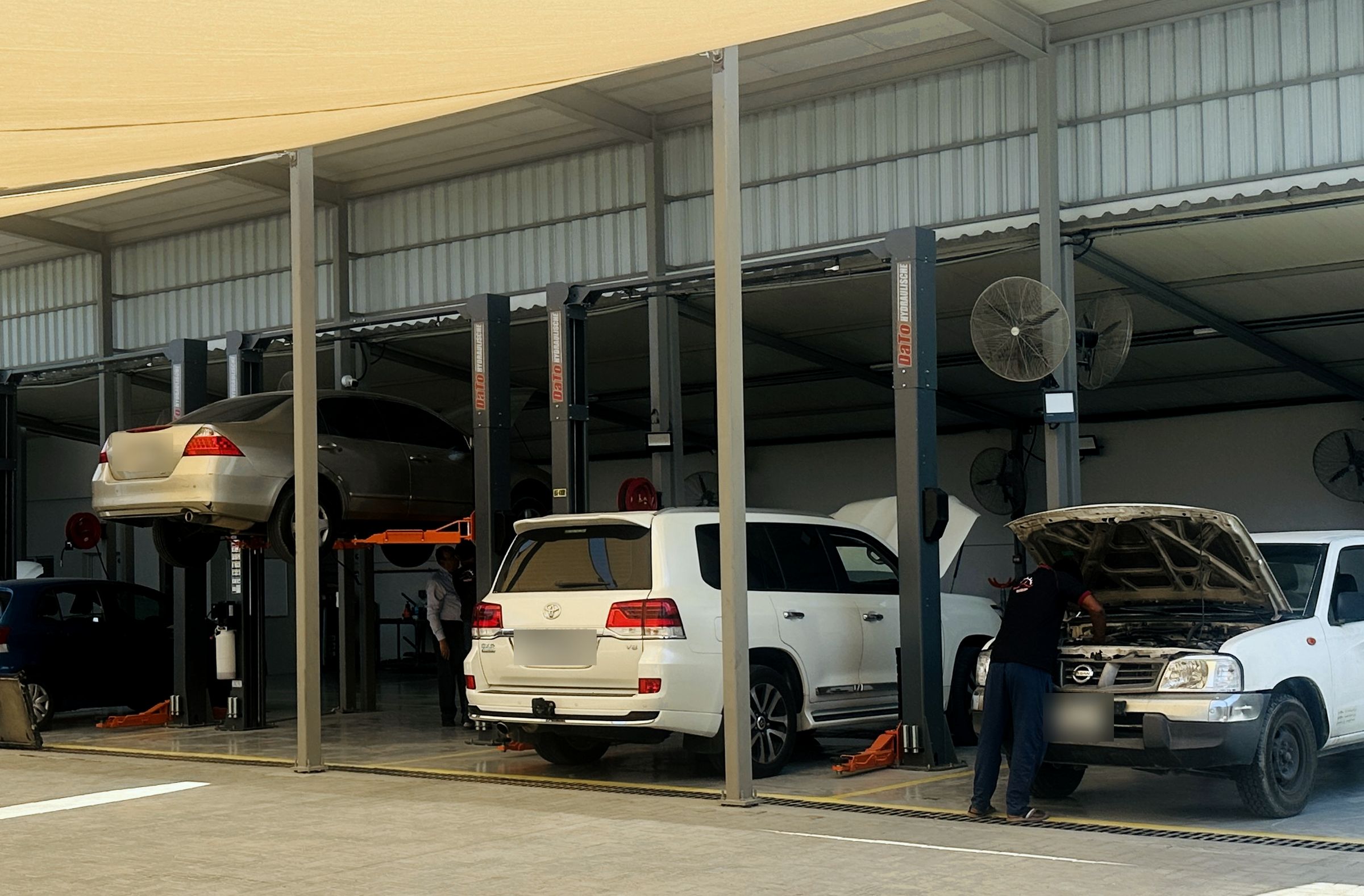 Toyota Land Cruiser and Nissan pickup in the service bays, with a sedan raised on a two-post lift