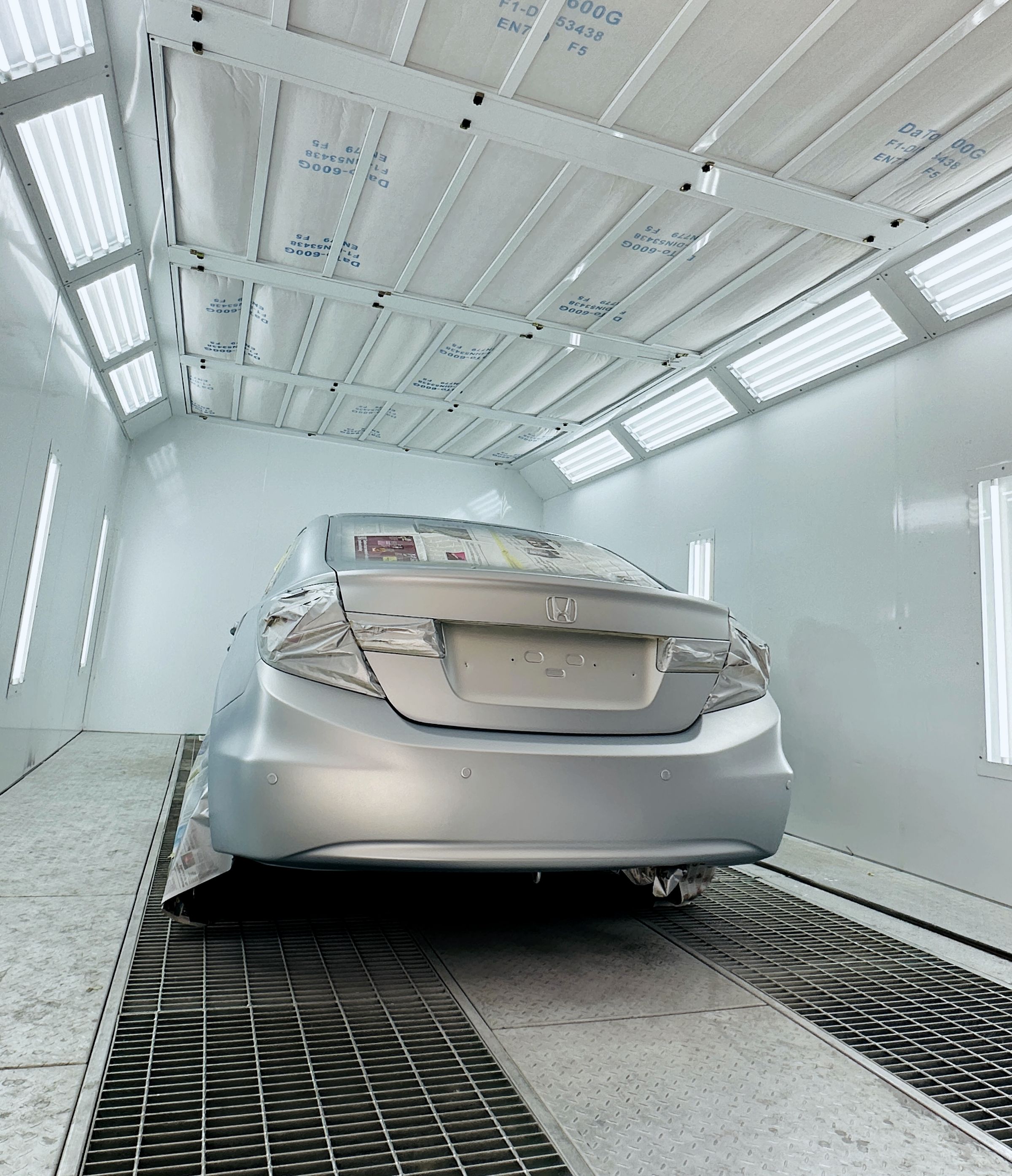 Rear of a car masked for a respray under the paint booth lights