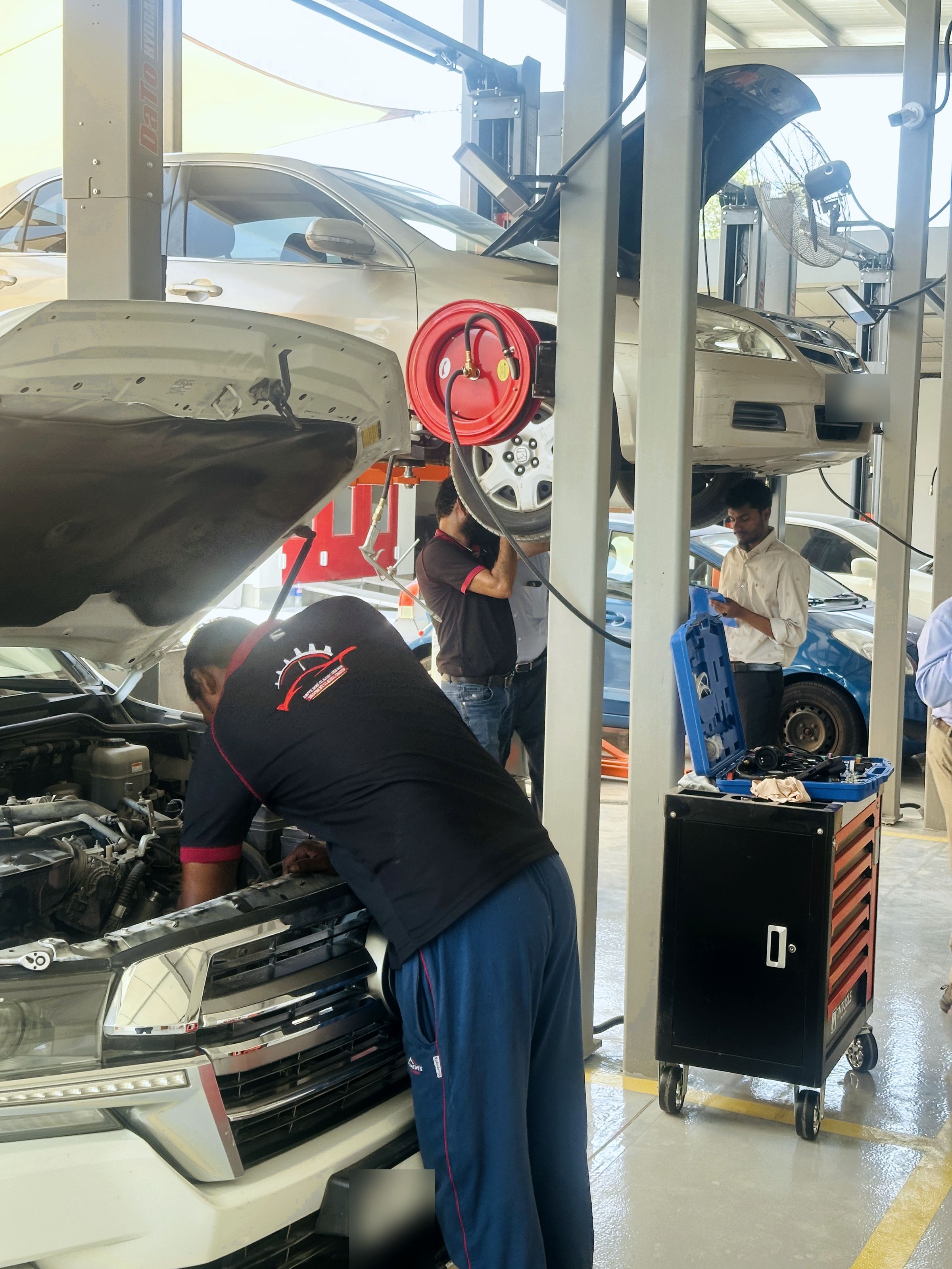 Uniformed technicians working on a Land Cruiser and a lifted sedan