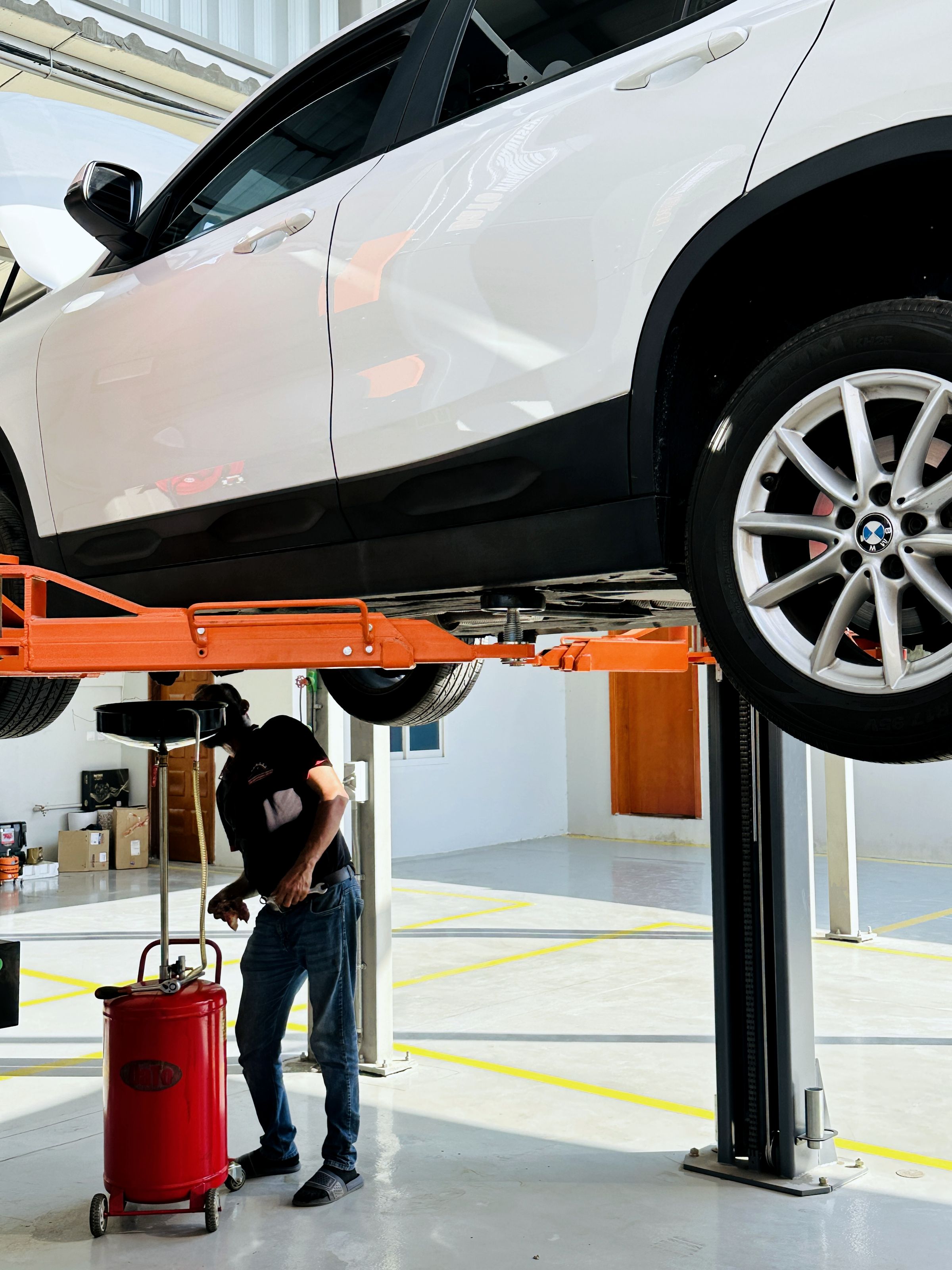 Technician draining engine oil from a BMW raised on a two-post lift