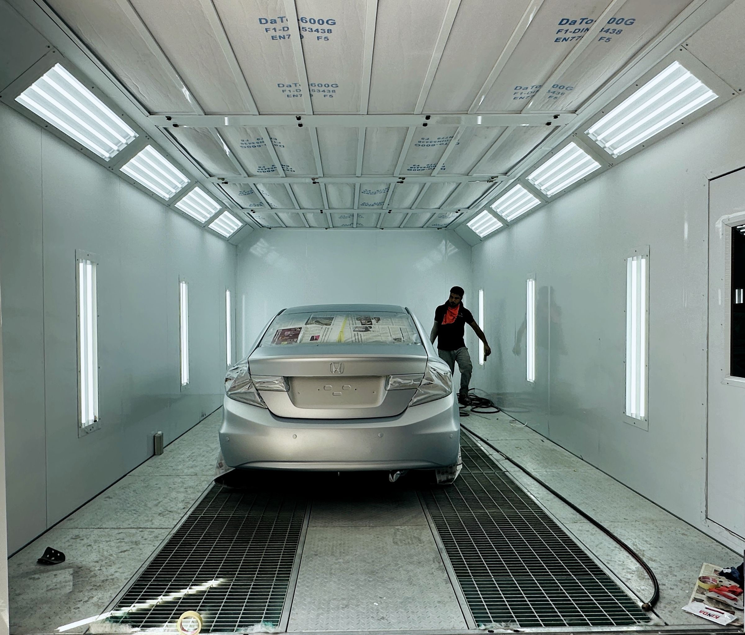 Car being resprayed inside the paint booth at our Al Qusais workshop, with the painter beside it