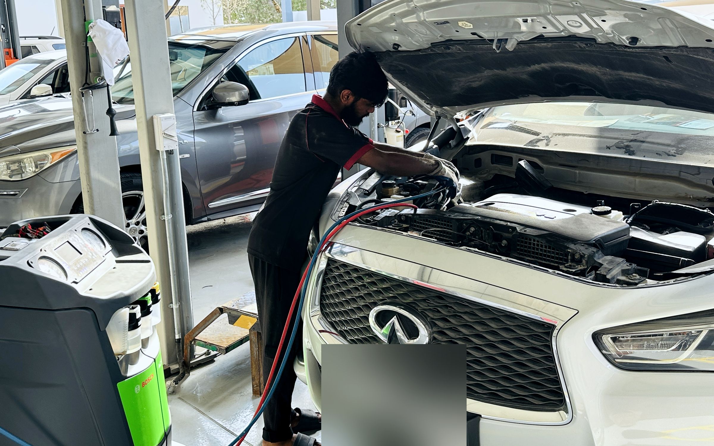 Technician servicing a car's air conditioning with a Bosch AC service machine