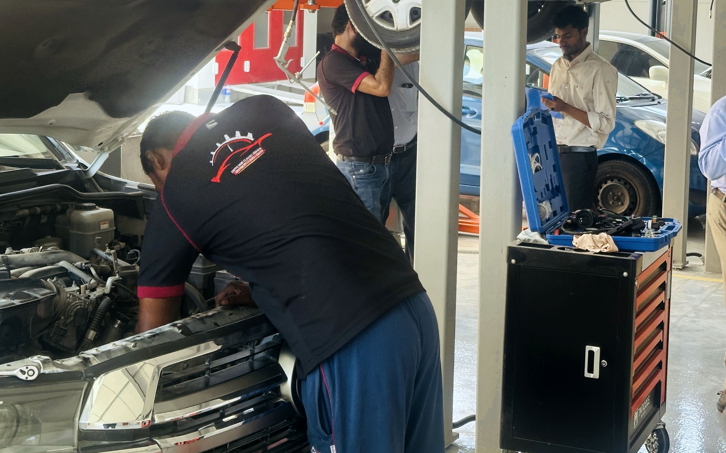 Technician working in the engine bay of a Land Cruiser with a sedan raised on the lift behind