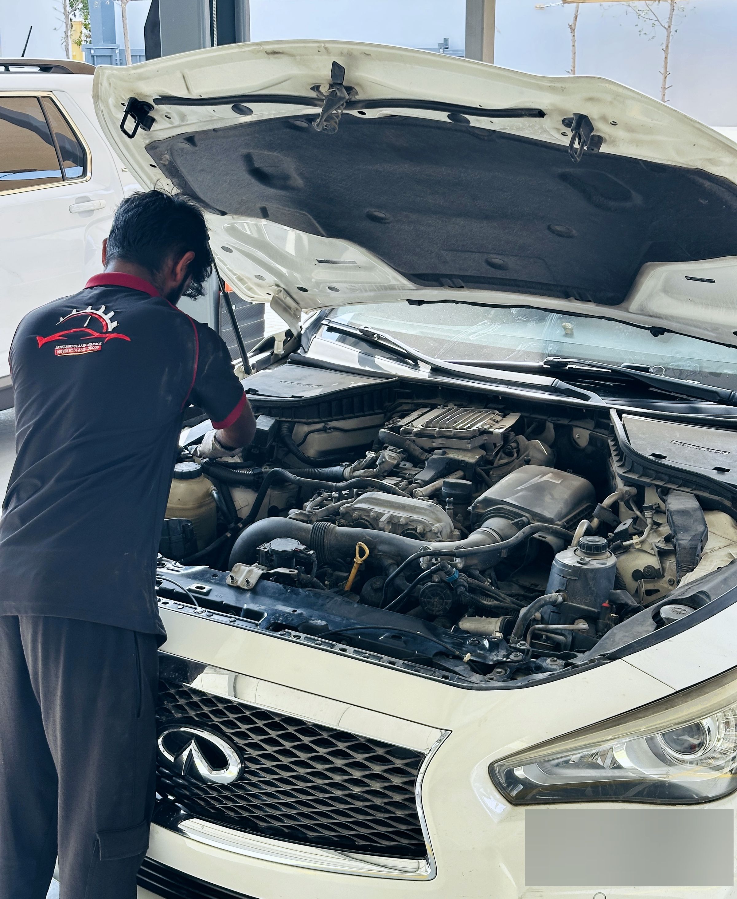 Technician in a Drive Way Classic Garage uniform working in the engine bay of an Infiniti